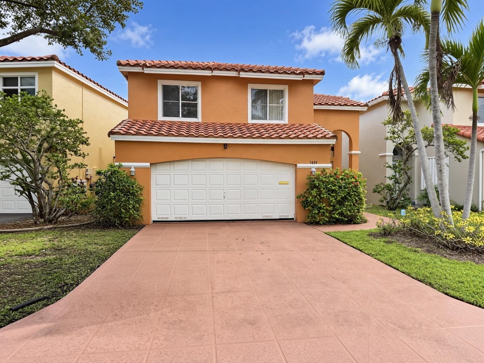 Two-story stucco exterior with a terra cotta tile roof, an integrated garage, a paved driveway, and mature landscaping