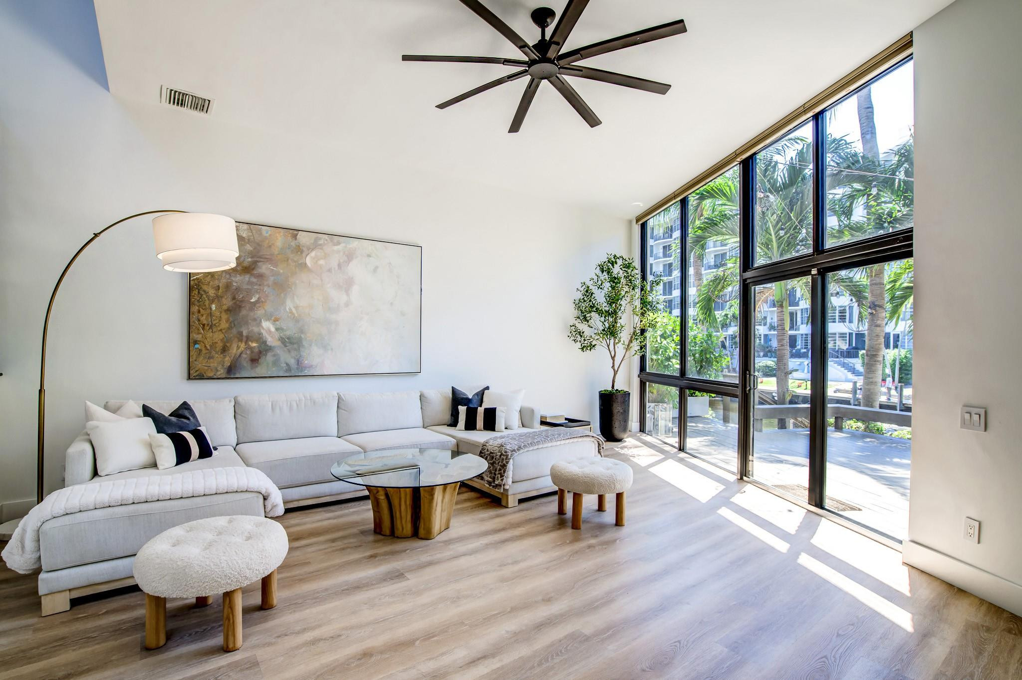 High ceilings, expansive floor-to-ceiling windows, wood-finish flooring, and a contemporary ceiling fan