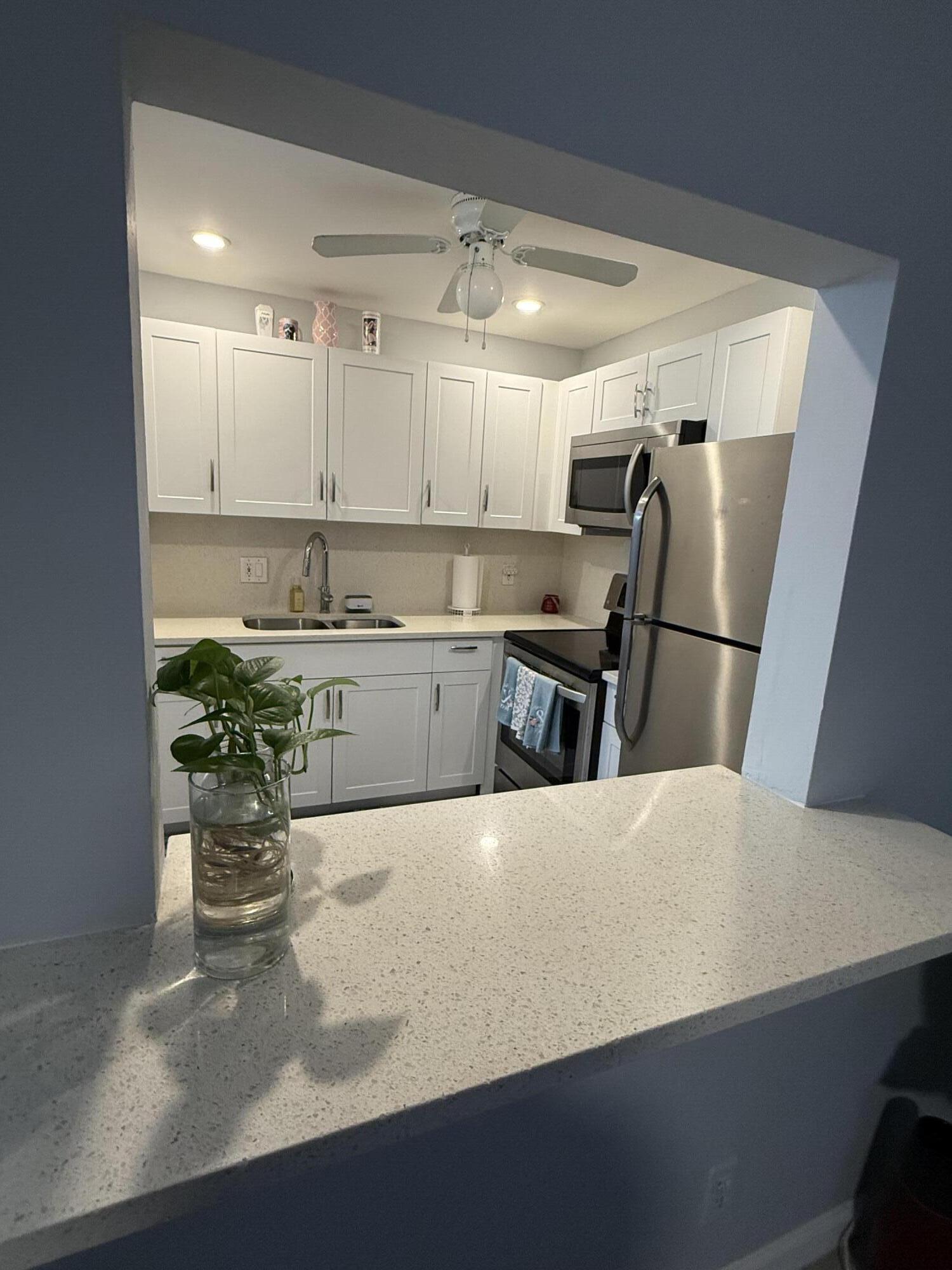 Kitchen featuring white cabinetry, stainless steel appliances, a white ceiling fan, recessed lighting, and a speckled light-toned countertop