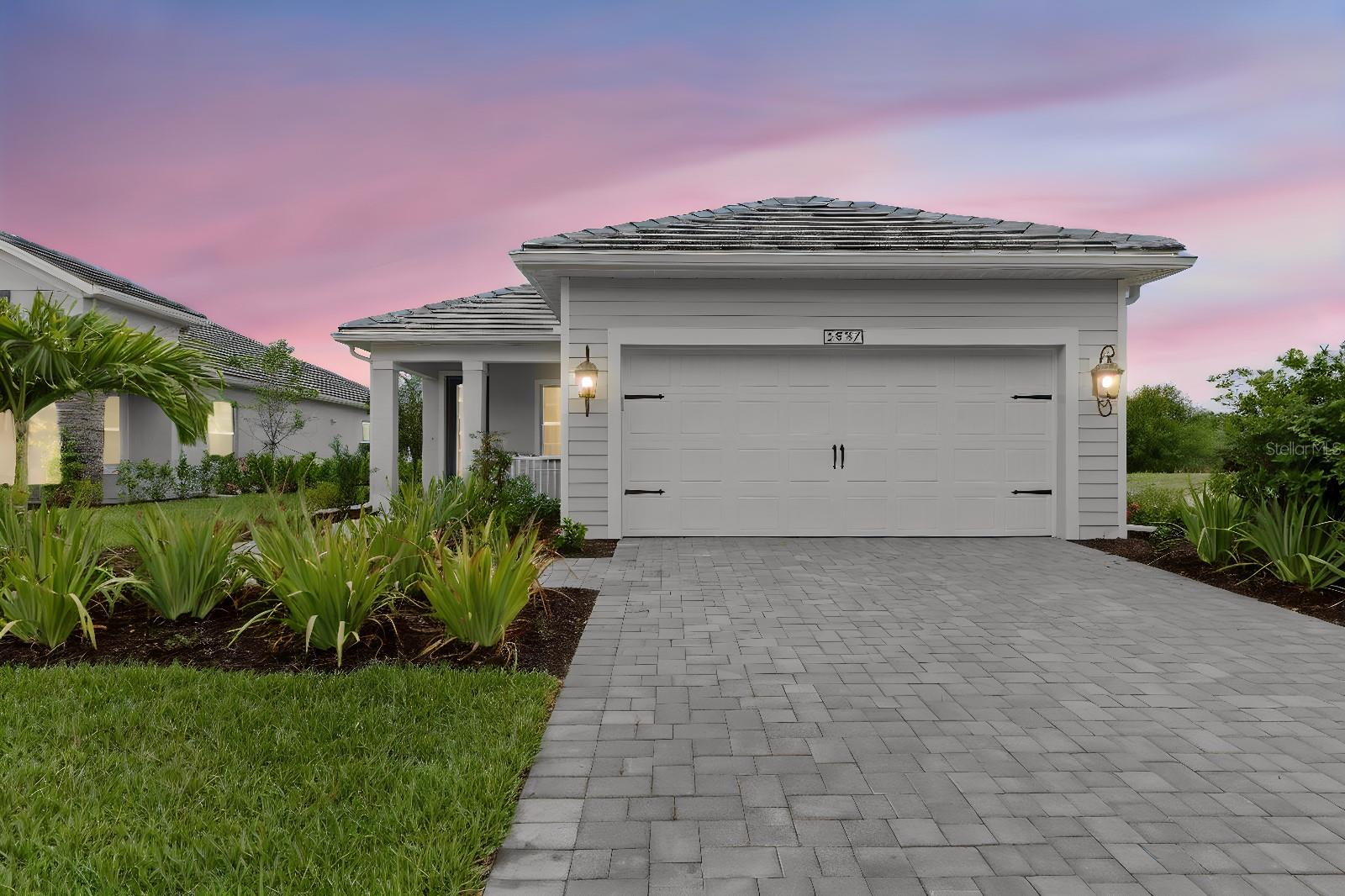 Front Exterior – Twilight curb appeal with a paver driveway and walkway leading to the two-car garage, framed by fresh landscaping under a soft sunset sky.