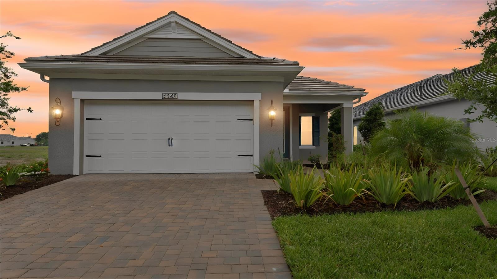 Front Exterior – A single-story Coastal elevation with a paver driveway, extended two-car garage, and tropical landscaping under a soft twilight sky.